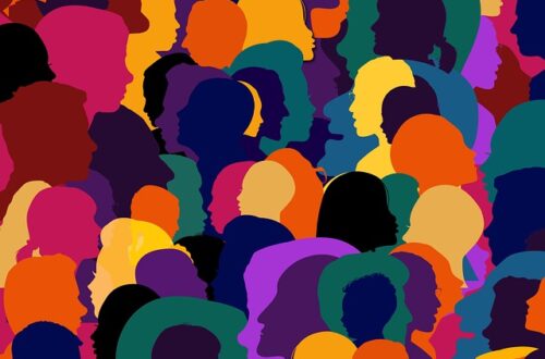 Eine digitale Illustration zeigt eine vielfältige Gruppe von Menschen mit unterschiedlich gefärbten Silhouetten und Gesichtern, die sich überlagern. Die Farben reichen von Blau, Grün und Gelb bis zu Rot, Lila und Orange. Die Köpfe sind in verschiedenen Größen und Richtungen angeordnet, was Vielfalt und Inklusion symbolisiert.