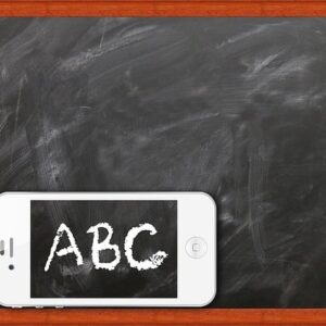 Ein Smartphone liegt vor einer Kreidetafel mit Holzrahmen. Auf dem Bildschirm des Smartphones ist in weißer Kreideschrift ‘ABC’ zu sehen – die Schrift passt optisch zur Tafel. Symbolbild für digitales Lernen oder Medienbildung in der Schule.