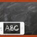 Ein Smartphone liegt vor einer Kreidetafel mit Holzrahmen. Auf dem Bildschirm des Smartphones ist in weißer Kreideschrift ‘ABC’ zu sehen – die Schrift passt optisch zur Tafel. Symbolbild für digitales Lernen oder Medienbildung in der Schule.