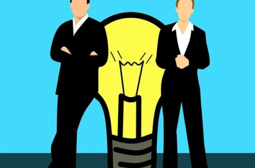 Illustration mit einem Mann und einer Frau in Businesskleidung, die jeweils auf einer Seite vor einer großen gelben Glühbirne stehen. Die Figuren haben keine Gesichtszüge. Die Glühbirne symbolisiert eine Idee oder Innovation – möglicherweise steht das Bild für Zusammenarbeit oder unterschiedliche Perspektiven bei der Lösungsfindung.